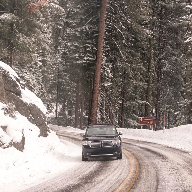 A black car drives down an icy and snowy road.