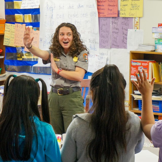 In a classroom, a park ranger raises her hand in the 