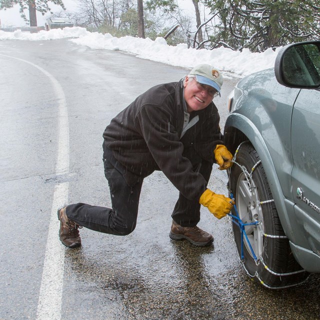 A man installs chains on his vehicle. Photo by Kirke Wrench.