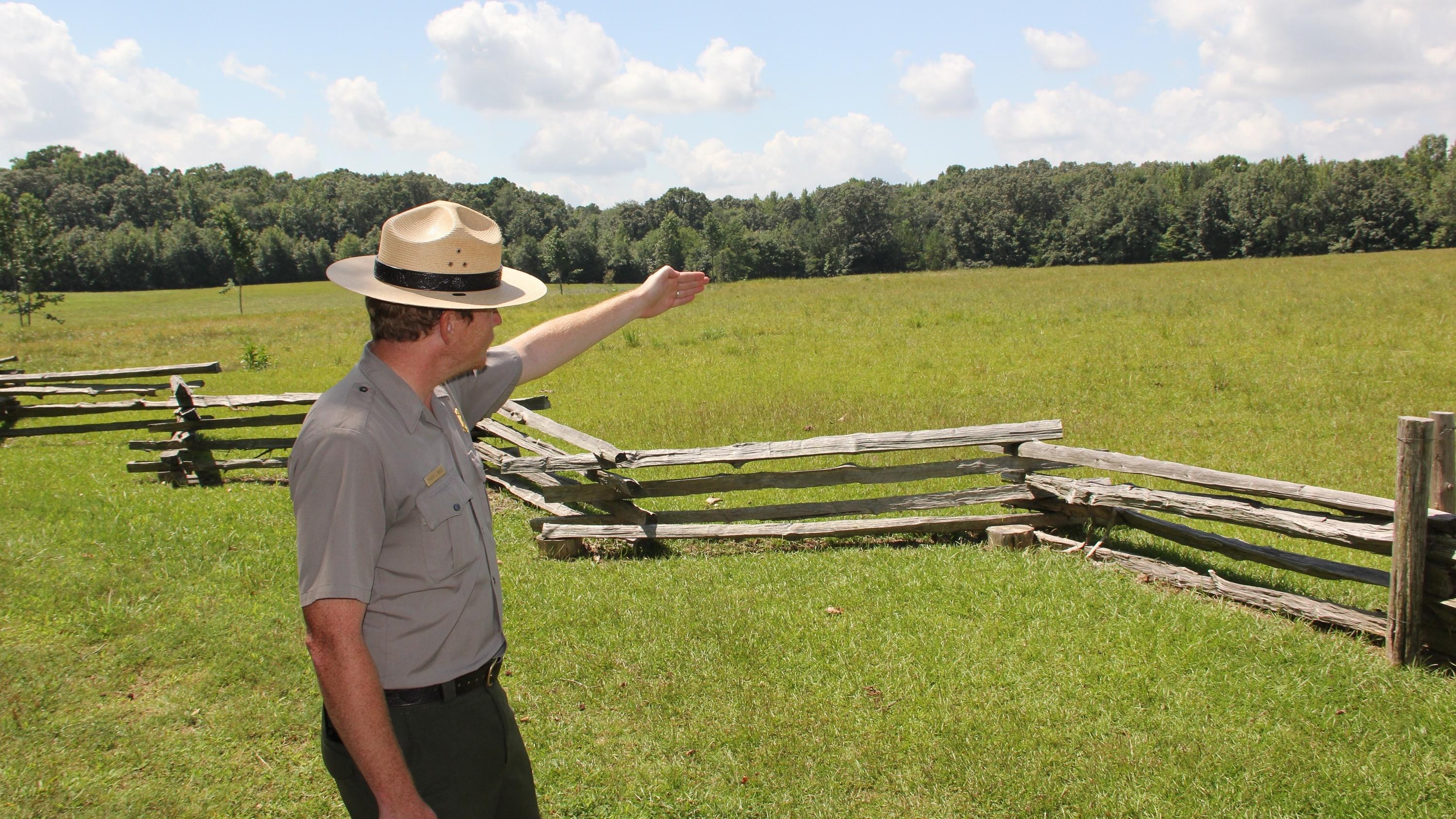 Park ranger in green and gray points to a field