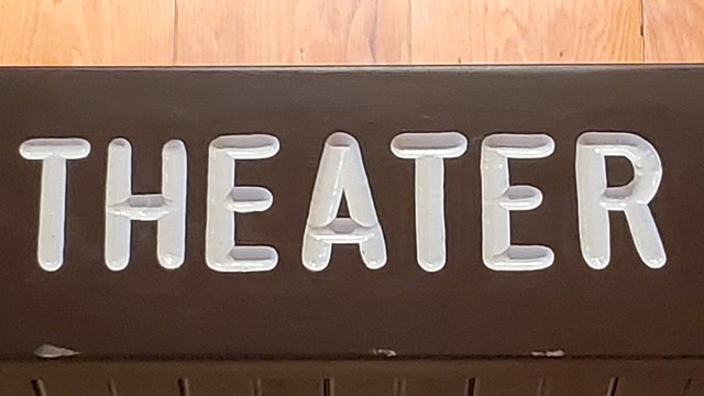A brown sign with white letters that says "Theater"