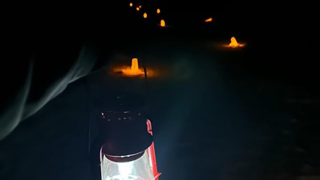 glowing luminaries light a trail while the arm of a ranger holds a lantern.