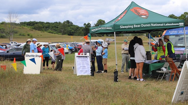 Event goers funnel in from a parking lot in a field as friendly rangers greet them. 