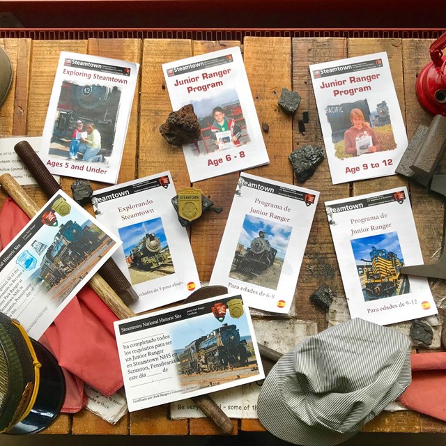 10 Junior Ranger activity books scattered on a table top along with train-related items