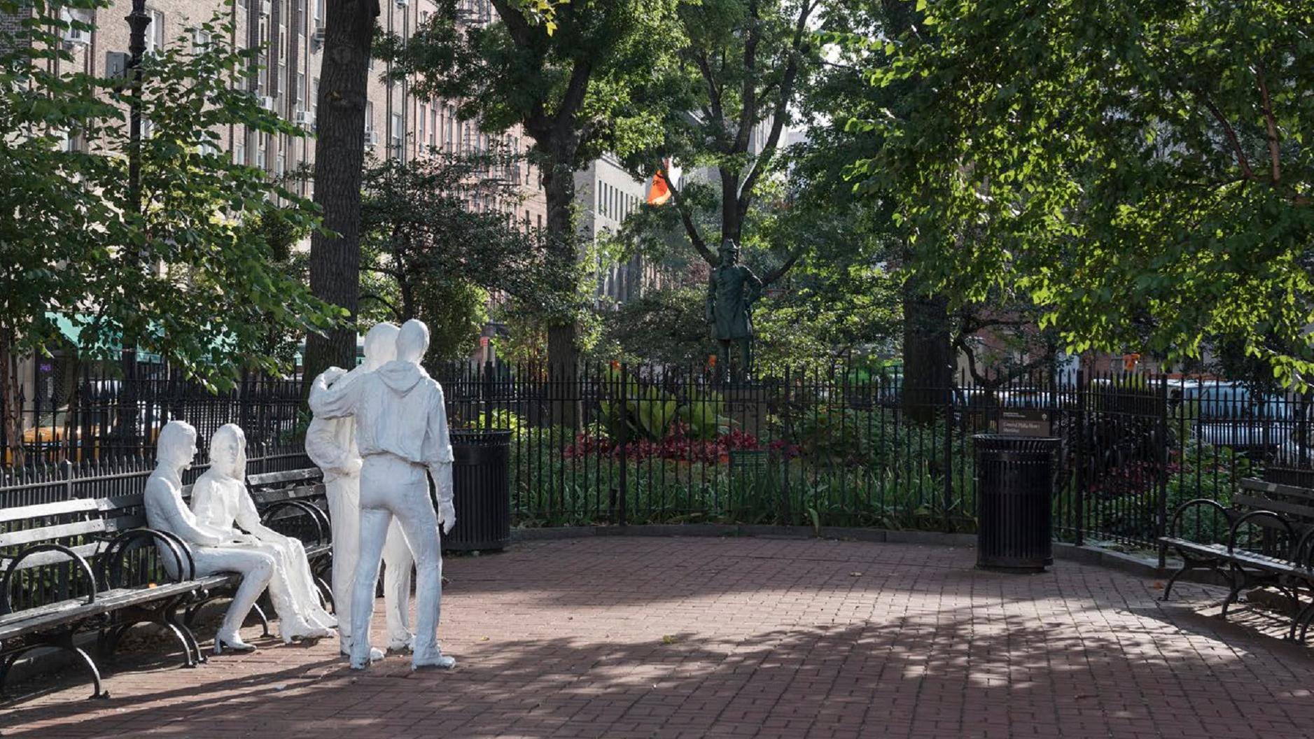 Christopher Park, surrounded by green benches, laid with brick, with two white statues in the center