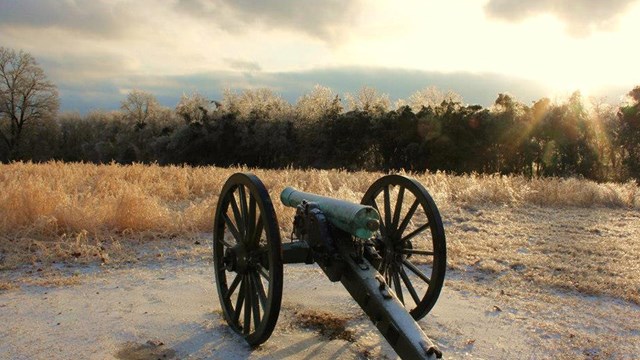 A cannon sits in the foreground of an ice covered field.