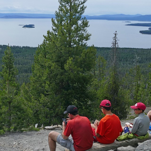 Hikers rest and look out at Yellowstone Lake from atop a mountaintop.