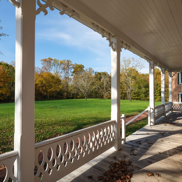 a wooden porch with wooden railing overlooking a green field with trees.