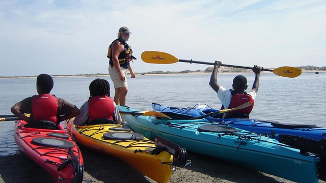 youth in kayaks on the beach with instructor at waters edge