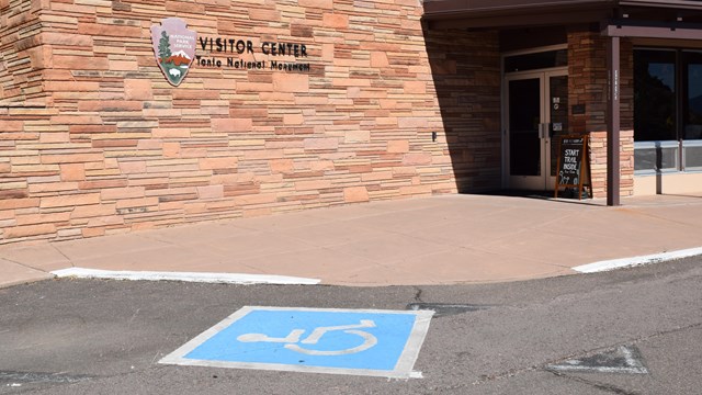 Parking space with a wheelchair logo painted on it near a door to a building.