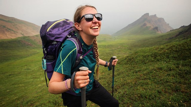 a smiling young woman with hiking backpack and poles