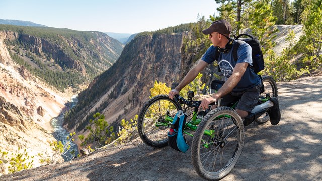a man using a mobility device looks at a view of a river canyon