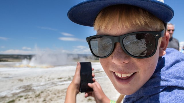 a child in sunglasses holds up a phone