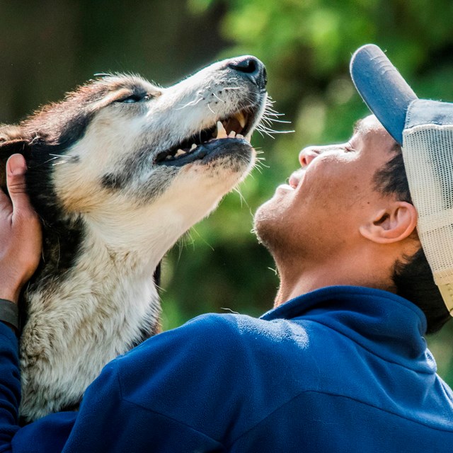 a man in a baseball hat pets a happy dog