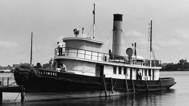 The Baltimore docked, on the water, people on it in the process of restoring it. 