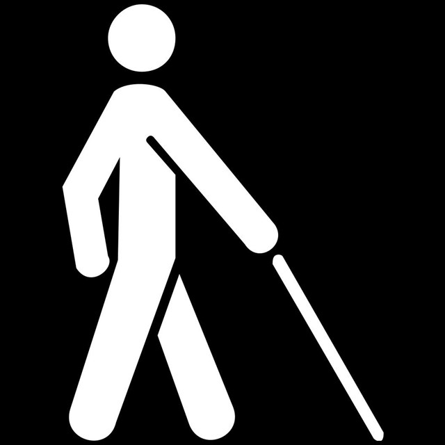 A black and white icon of a person with a seeing-eye cane.