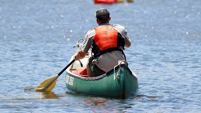 park ranger in life vest paddling in canoe on the water with back to the camera