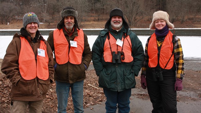 Four volunteers in thick winter clothing smiling in front of frozen river.