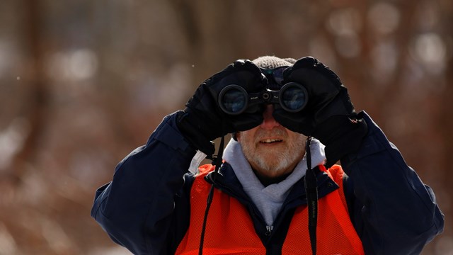 Person looking through binoculars, straight at camera.