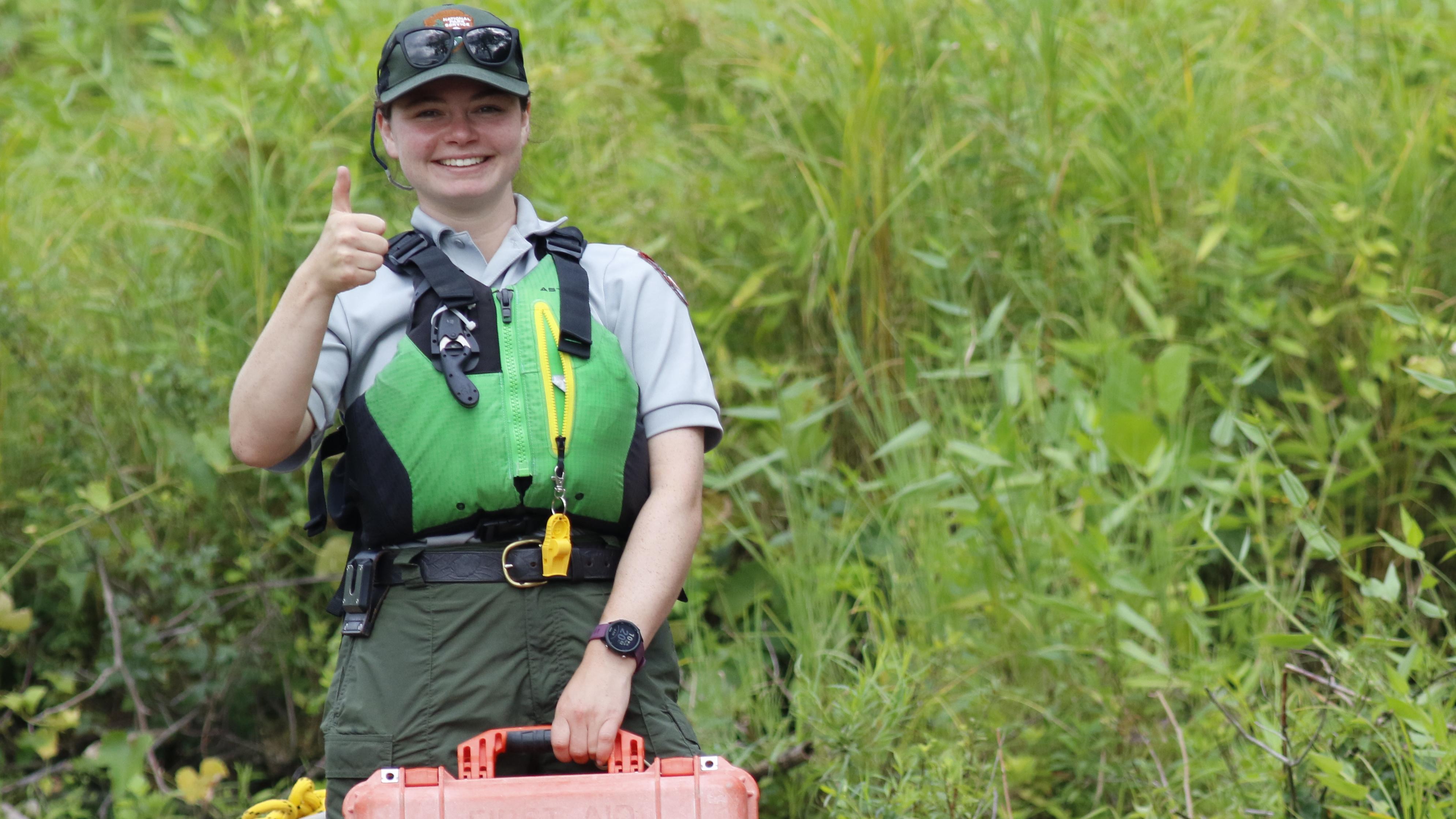 Park Ranger in life jacket smiles at camera while holding first aid kit.