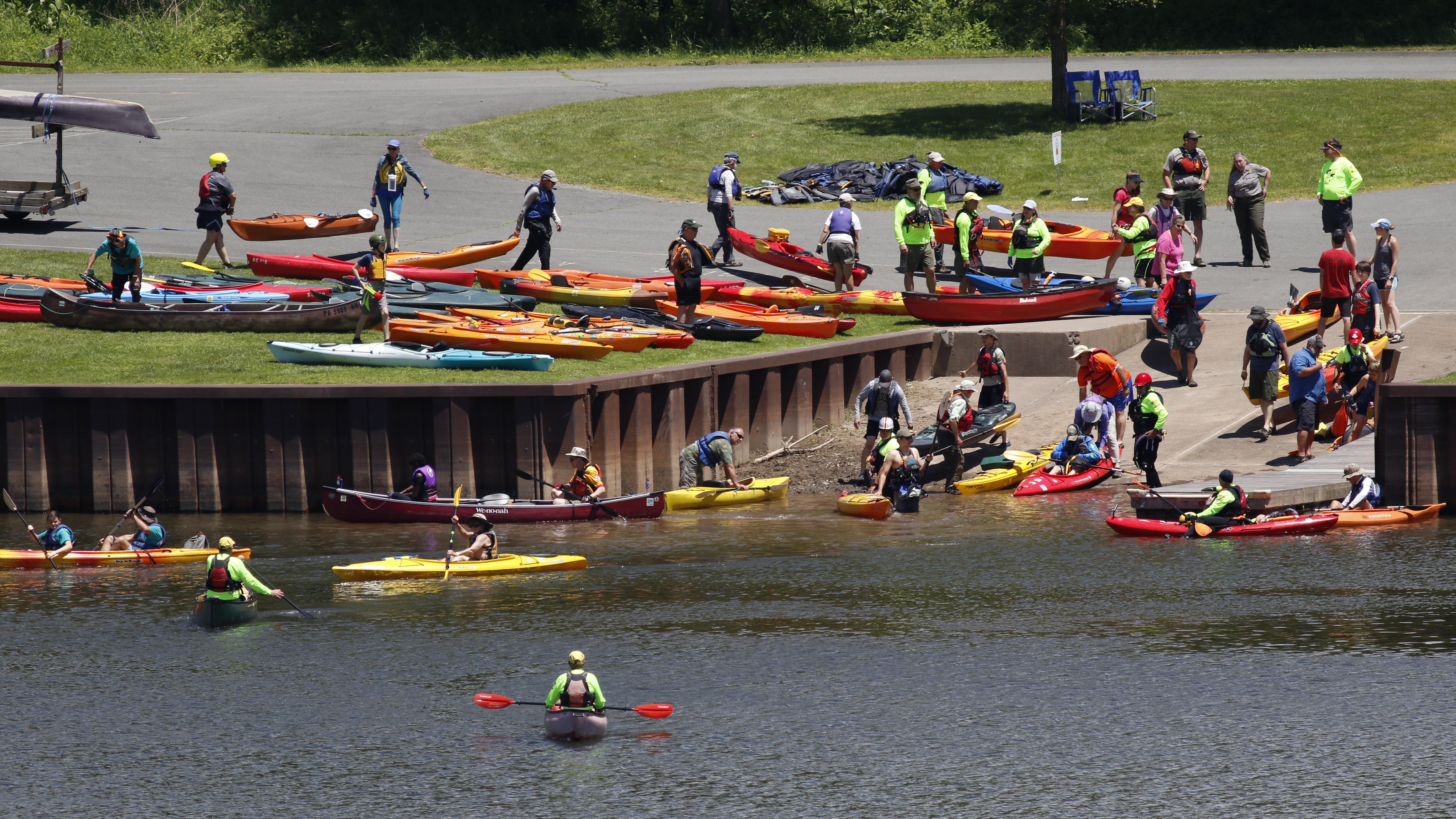 Public access area into a river. Paved ramp inclines into the river. People with kayaks enter water.
