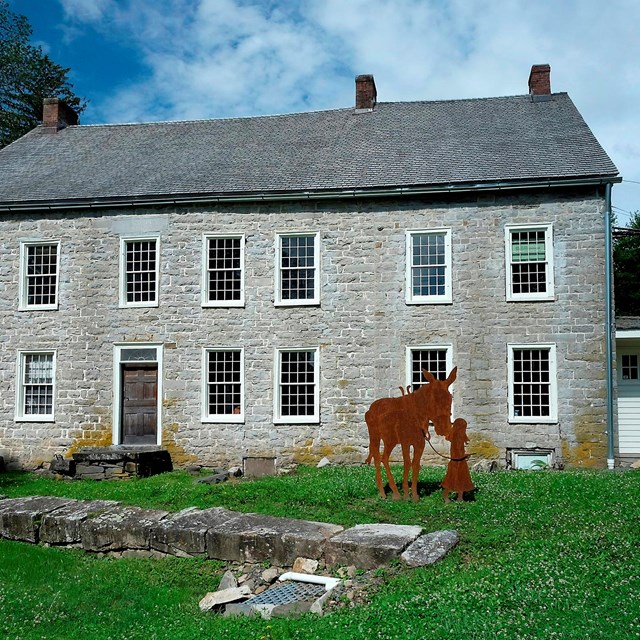 Stone building with metal silhouette of a child leading a mule.