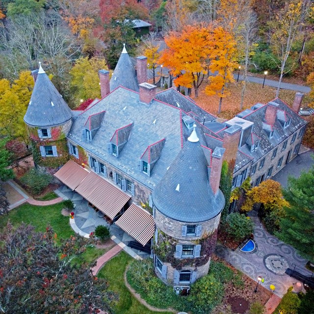 Bird's eye view: Grand stone 3-story mansion with turrets/towers in 3 corners and multiple chimneys.
