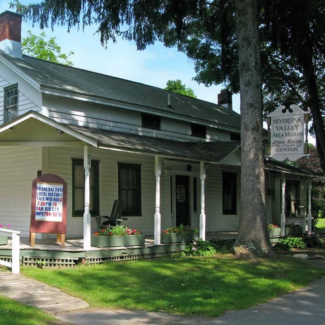 White 2-story house with wraparound covered porch and green trim.