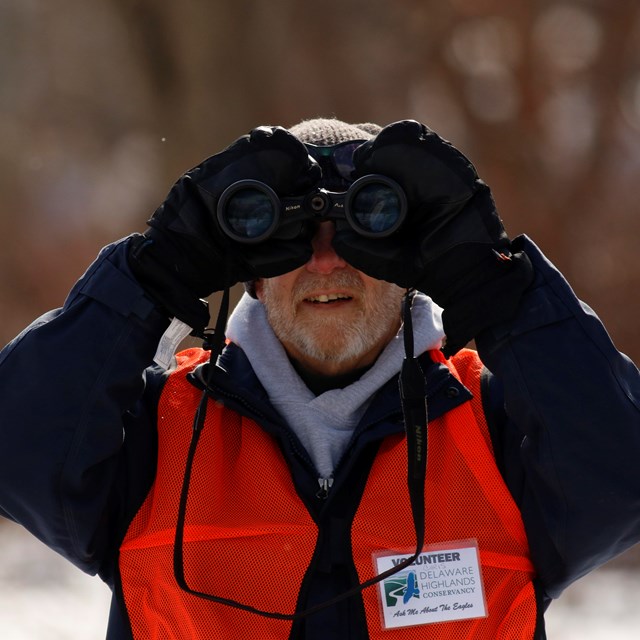 Person looking through binoculars, straight at camera.