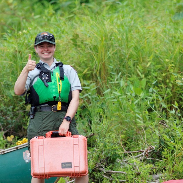 Park Ranger in life jacket smiles at camera while holding first aid kit.