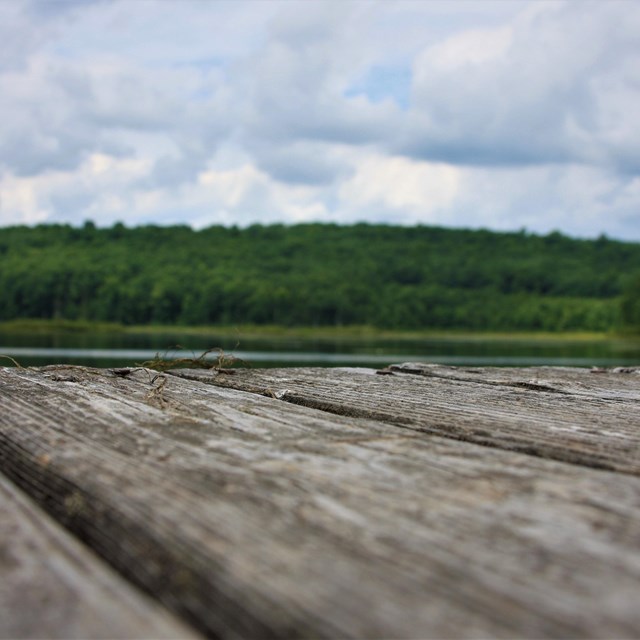 Photo from ground/low perspective of wooden boards of a dock. Emerald green hills are in distance.
