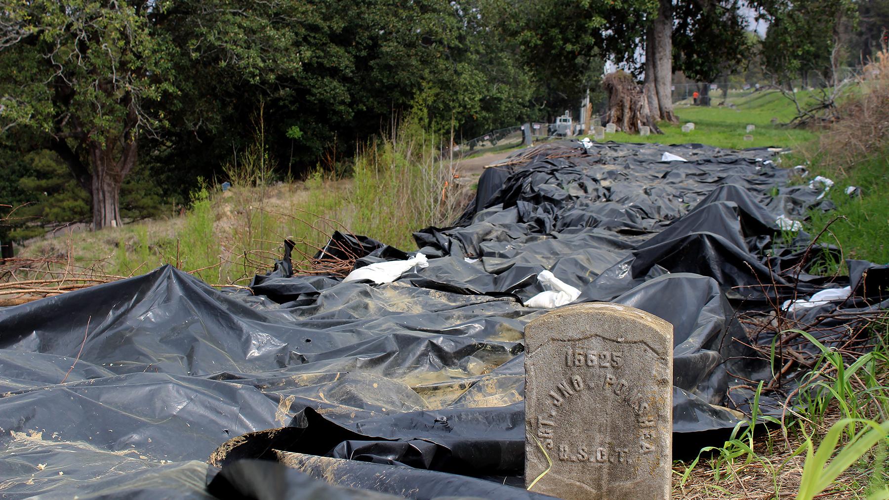 Large black tarps lay near a headstone in an affected area in the National Cemetery. 