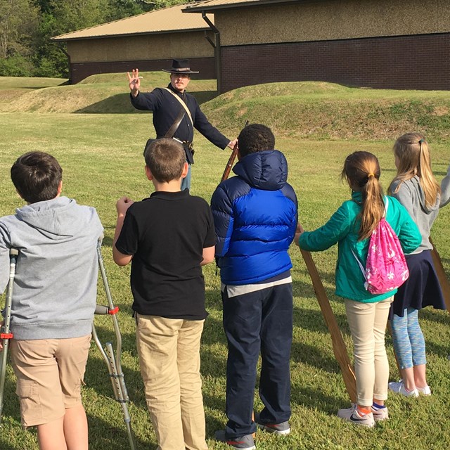 A park ranger dressed as a Union soldier teaching school children how to hold wooden muskets.