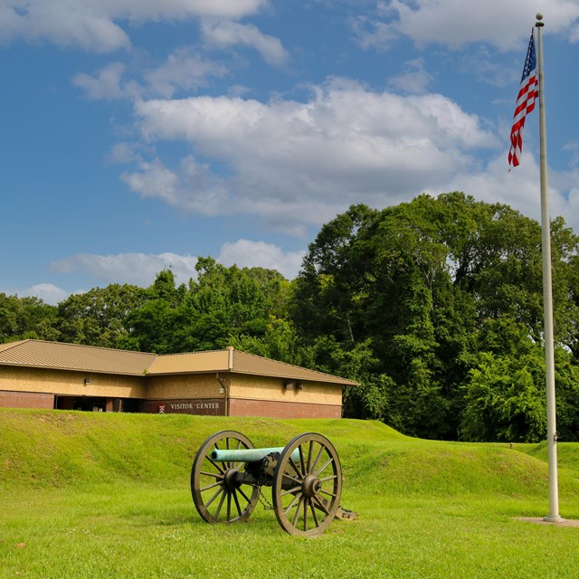 The Park Visitor Center sits near a hill with a flagpole and cannon in the foreground