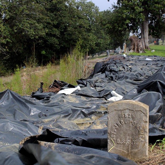 Large black tarps lay near a headstone in an affected area in the National Cemetery. 