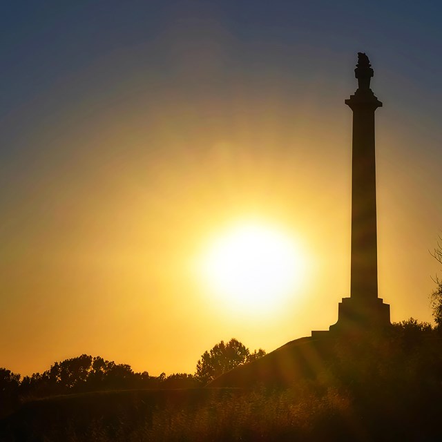 A monument in the foreground with the sunset behind