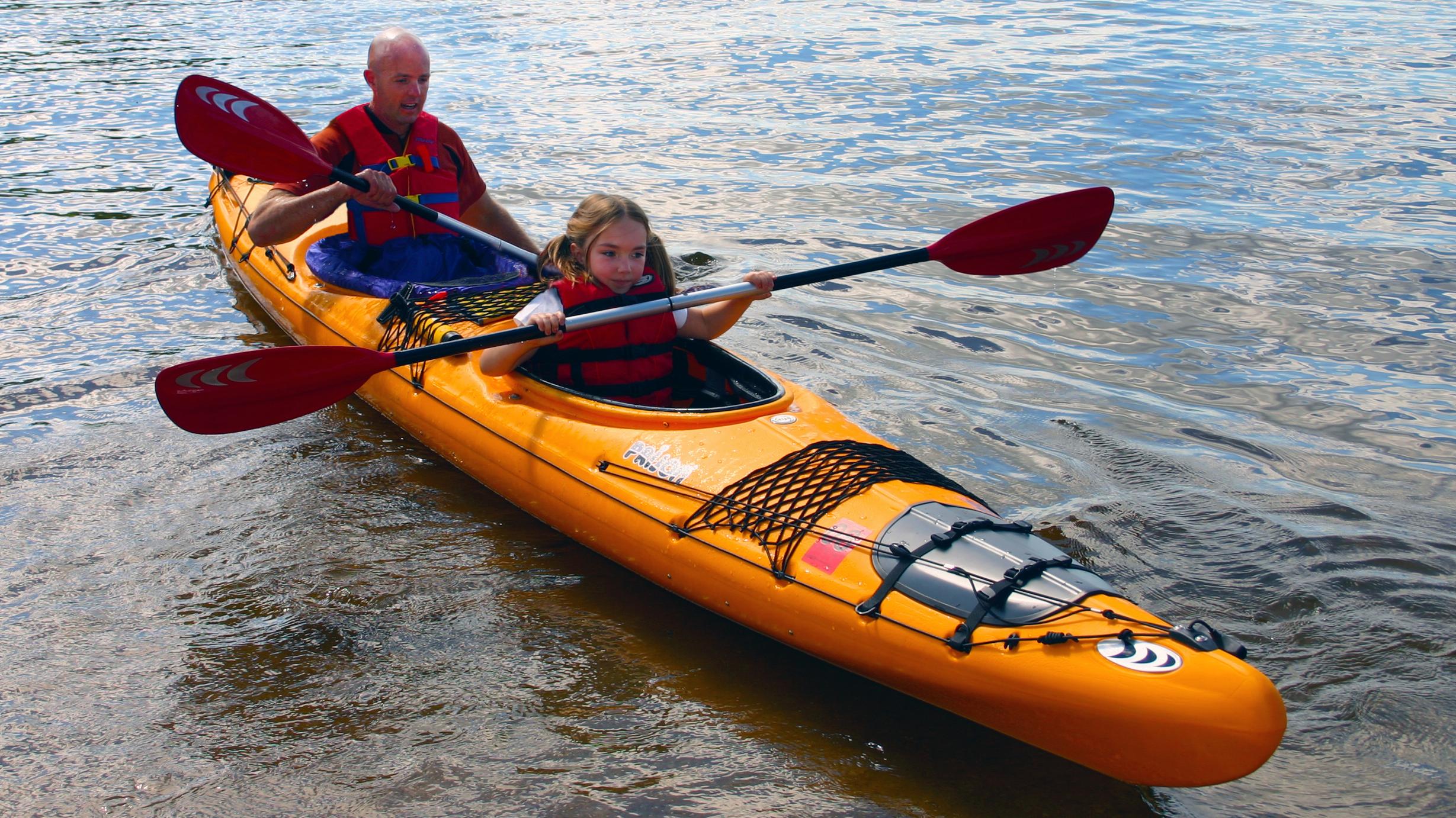 A bright yellow kayak floats near the shore, paddled by a young girl and her father.