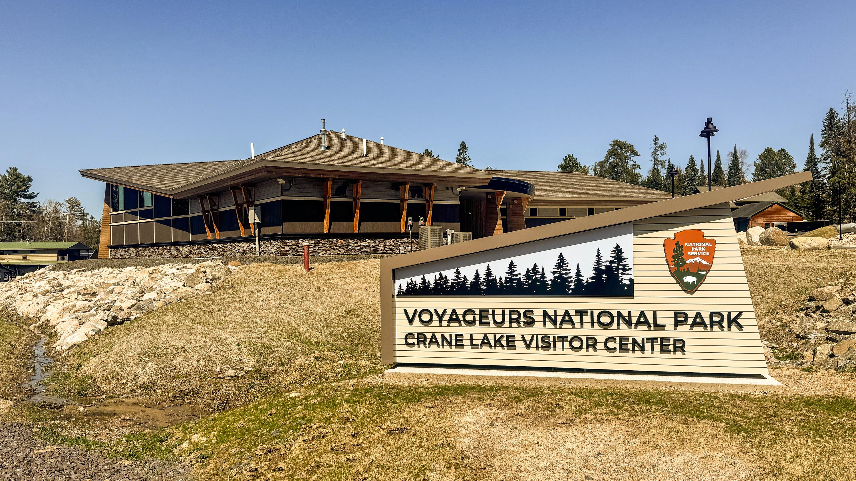 Photograph of NPS sign with "Voyageurs National Park Crane Lake Visitor Center" in the foreground. 