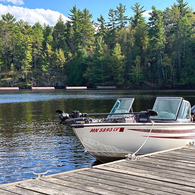 A white boat with red stripes shines in the sun, docked in a picturesque bay.