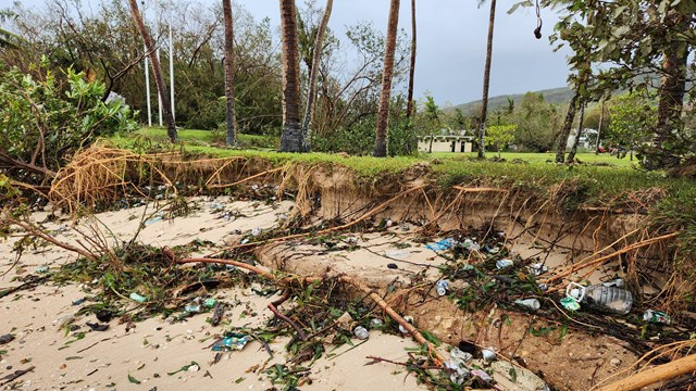 A badly eroded beach front covered in tree debris and trash