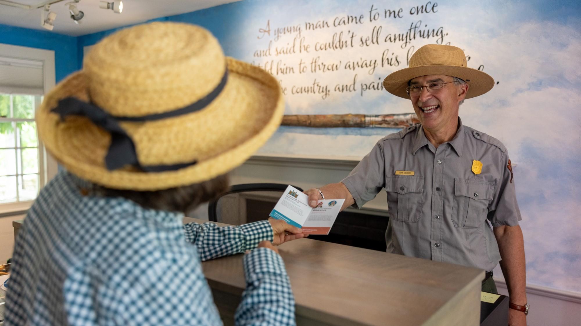 A park ranger hands a brochure to a visitor in the Weir Farm visitor center