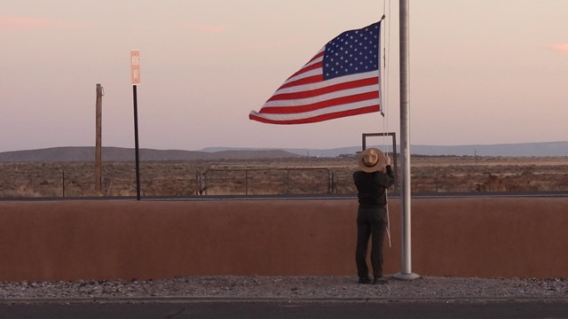 A uniformed park ranger shown from behind lowering the American flag