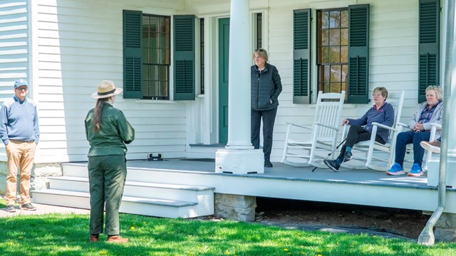 A ranger standing in front of a porch speaking to people.