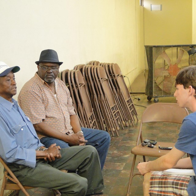 young white man on right talking to two black men on left