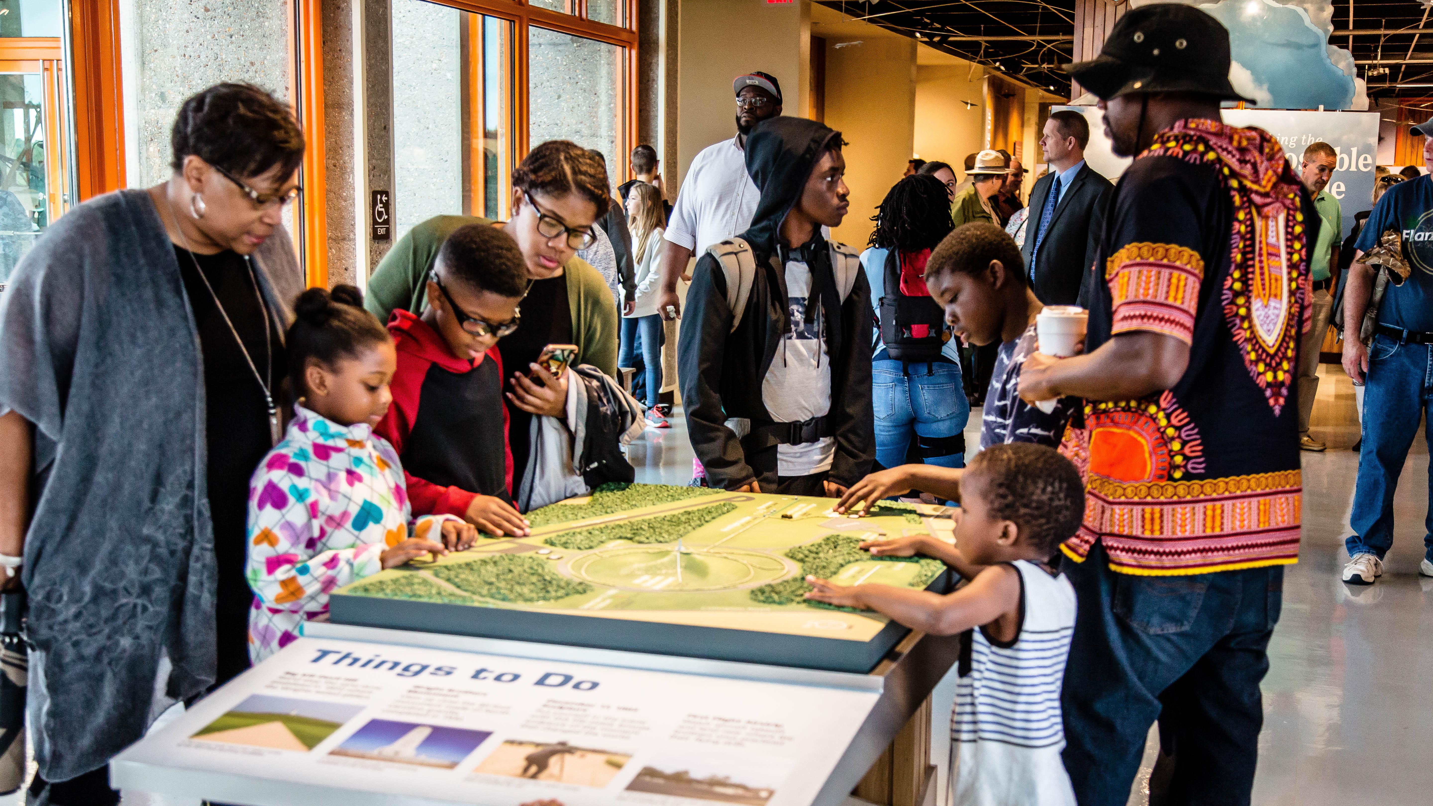 A group of people standing around a tactile map of Wright Brothers National Memorial