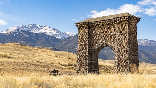 A large stone arch, Roosevelt Arch, stands in the foreground of a snow-capped mountain.