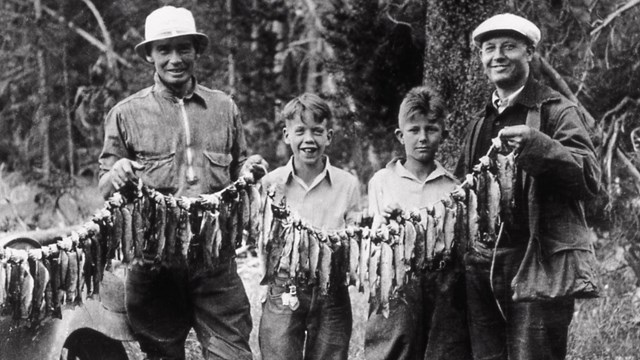 Historic image of 2 men with 2 boys, holding a line of fish they caught.