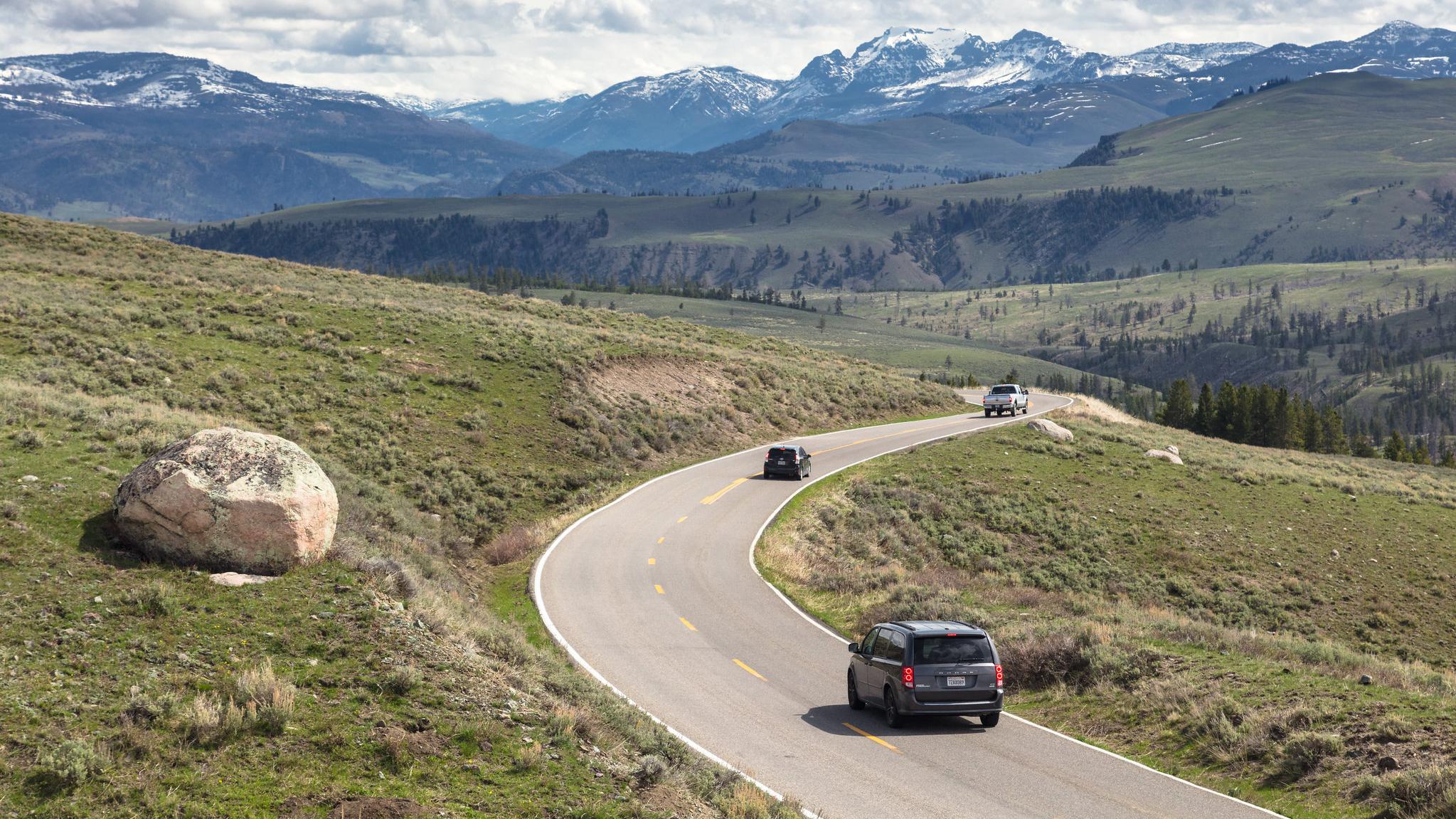 Cars drive through a winding road with mountains in the background.