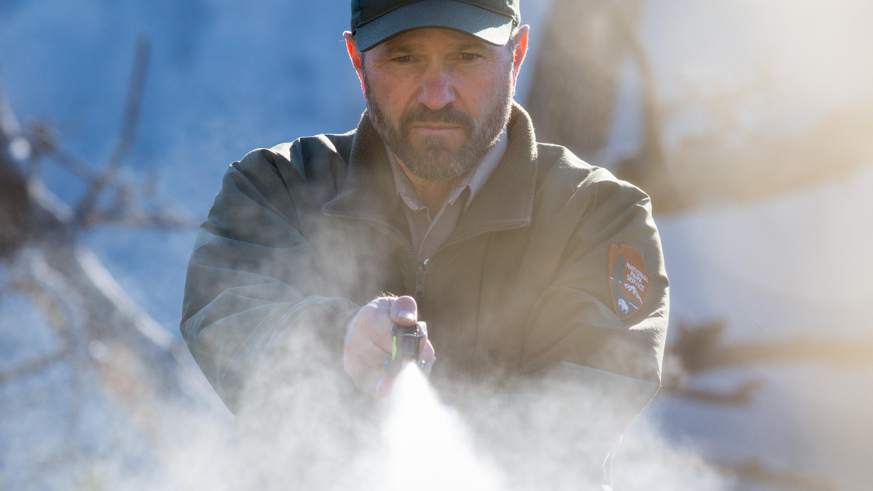 A park ranger sprays bear spray in a mist in front of him. 