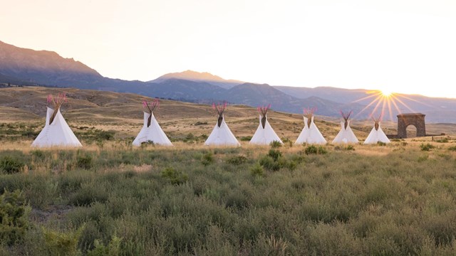 Row of teepees and stone arch at sunset